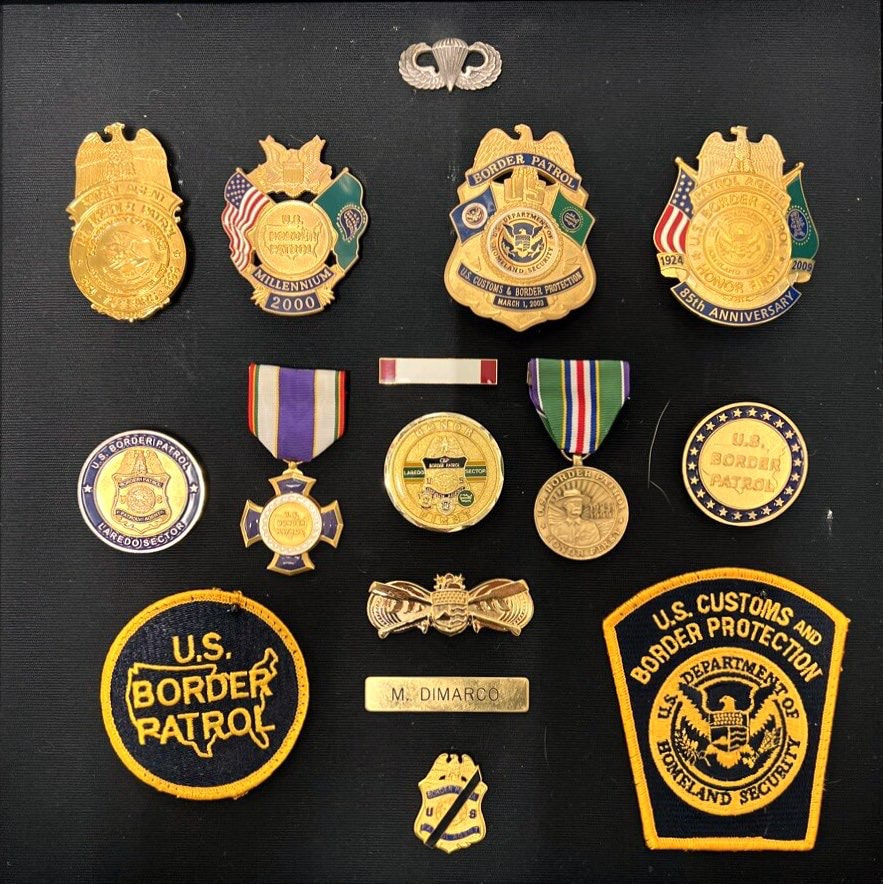 Agent Di Marco's shadow box including his U.S. Army Parachutist Badge, commemorative badges, Commissioner's Humanitarian Award, USBP Purple Cross Medal and more.