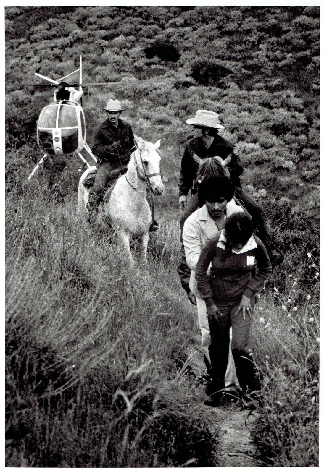 This 1970s/80s photo captures a poignant moment at the US border, where a couple seeking a new life are halted by horse-mounted agents, with a helicopter in the backdrop symbolizing the clash between tradition and modern immigration enforcement.