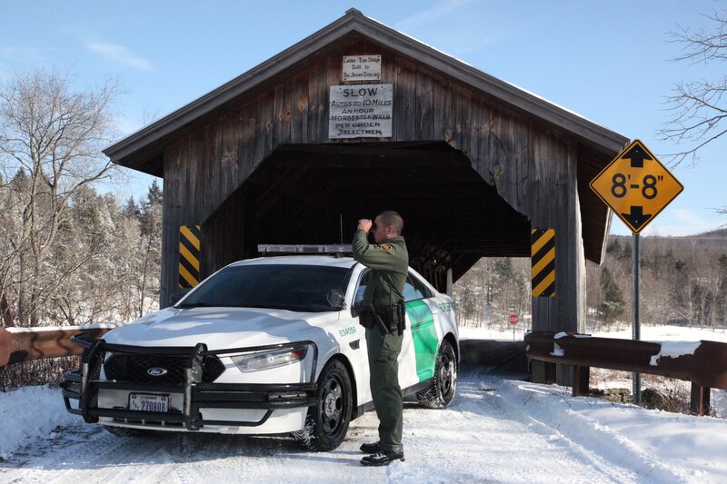 Border Patrol USBP miscellaneous modern agent with binoculars standing in front of his car near a covered bridge