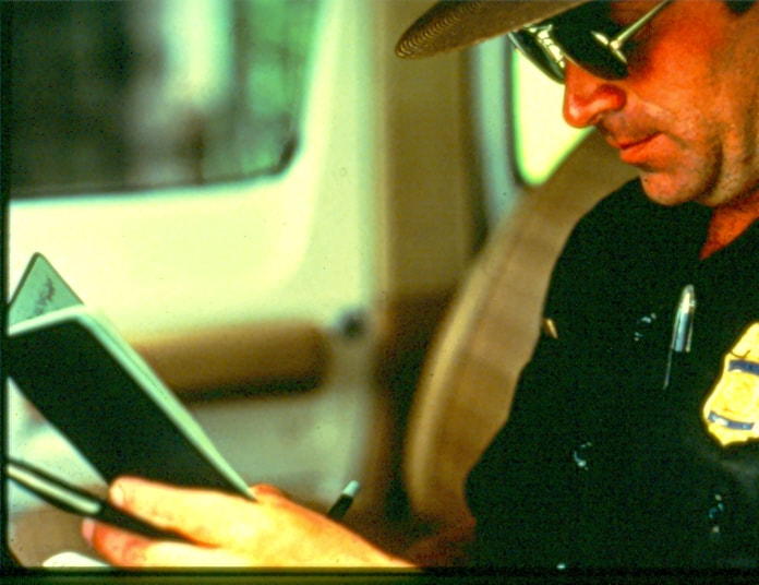 USBP Border Patrol photographs 1970-1990, agent reading a notebook in a car