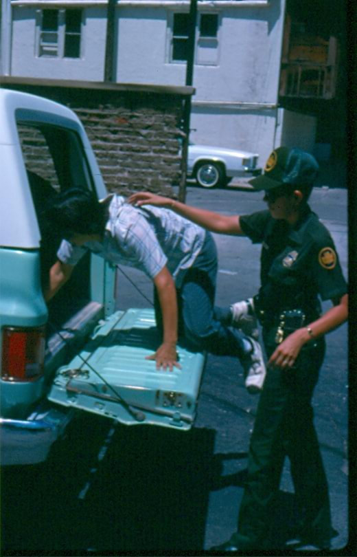 USBP Border Patrol photographs 1970-1990 an agent putting an arrested alien in the back of a sea foam green SUV