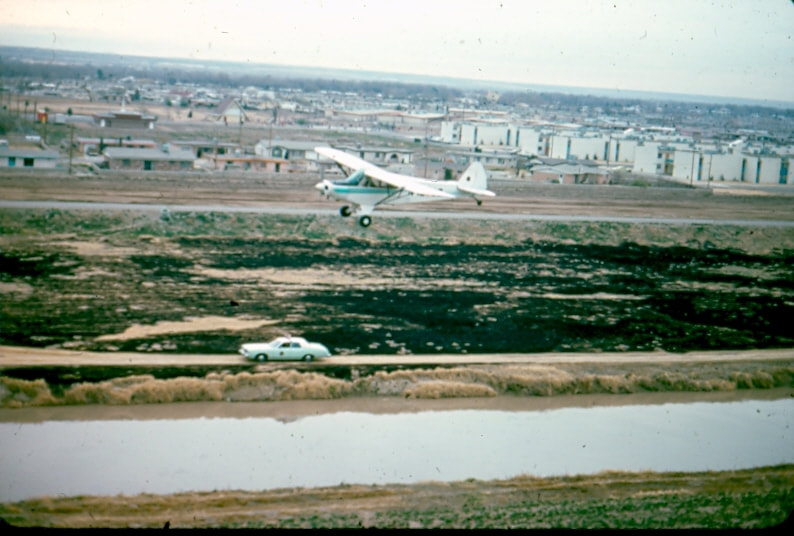 USBP Border Patrol photographs 1970-1990 a low flying USBP airplane with a USBP sea foam green car on the ground