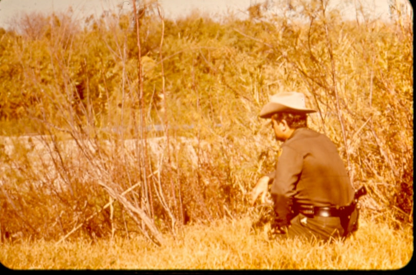 USBP Border Patrol photographs 1970-1990 an agent wearing a cowboy hat, kneeling and watching