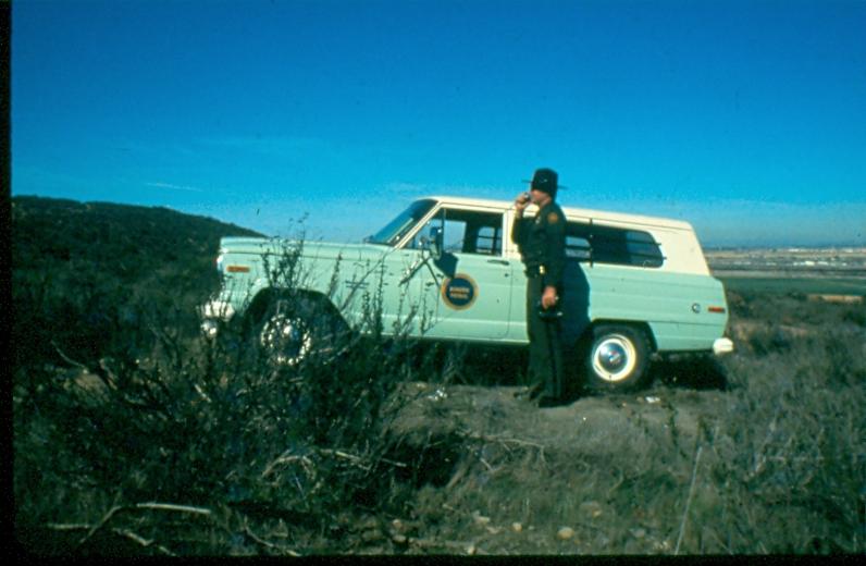 USBP Border Patrol photographs 1970-1990 an agent wearing a dress uniform standing next to a sea foam green SUV