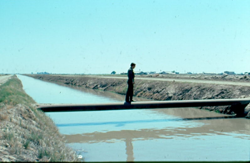 USBP Border Patrol photographs 1970-1990 agent crossing an irrigation ditch by walking over a pipe