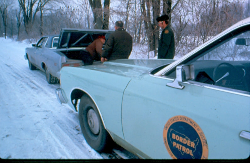 USBP Border Patrol photographs 1970-1990 agent helping people in the snow in front a sea foam green vehicle