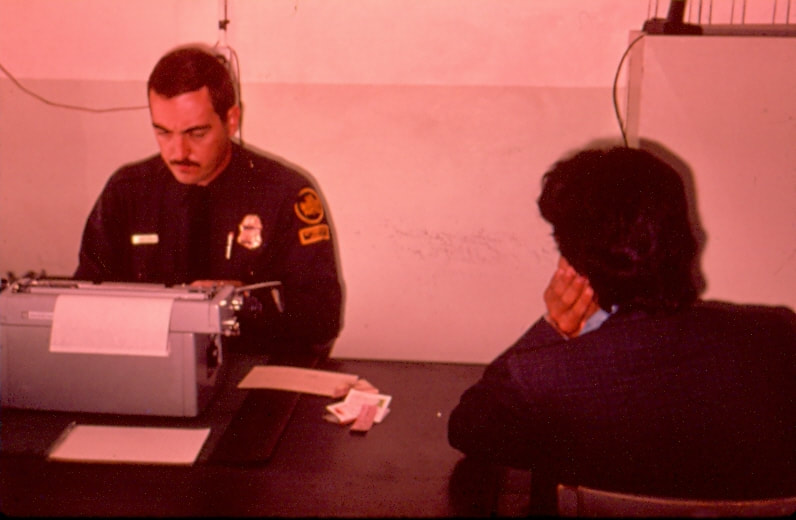 USBP Border Patrol photographs 1970-1990 agent wearing the 50th anniversary patch processing an alien