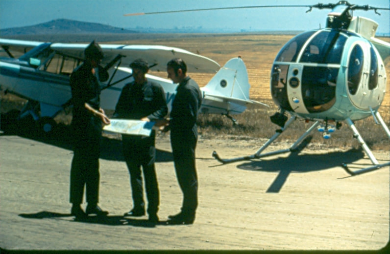 USBP Border Patrol photographs 1970-1990 agents  pilots standing between an airplane and a helicopter