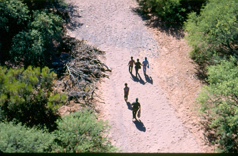 USBP Border Patrol photographs 1970-1990 aerial photo of an agent arresting a group and walking on a dirt road 
