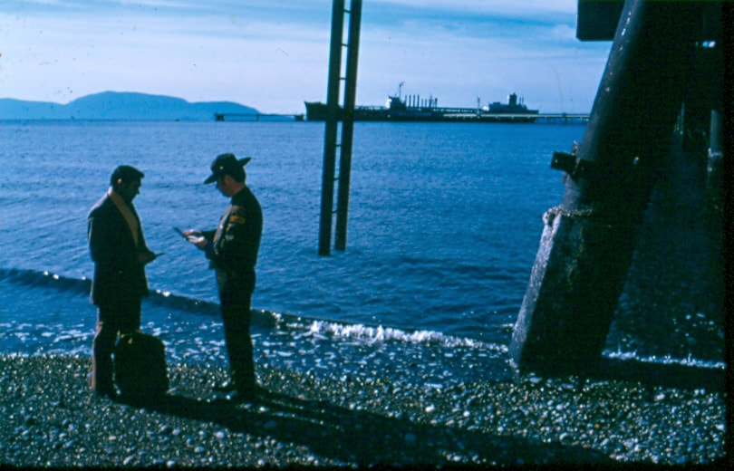 USBP Border Patrol photographs 1970-1990  agent wearing a dress uniform checking a man near the shoreline